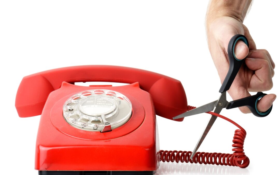 a pair of scissors cuts a line on a red telephone